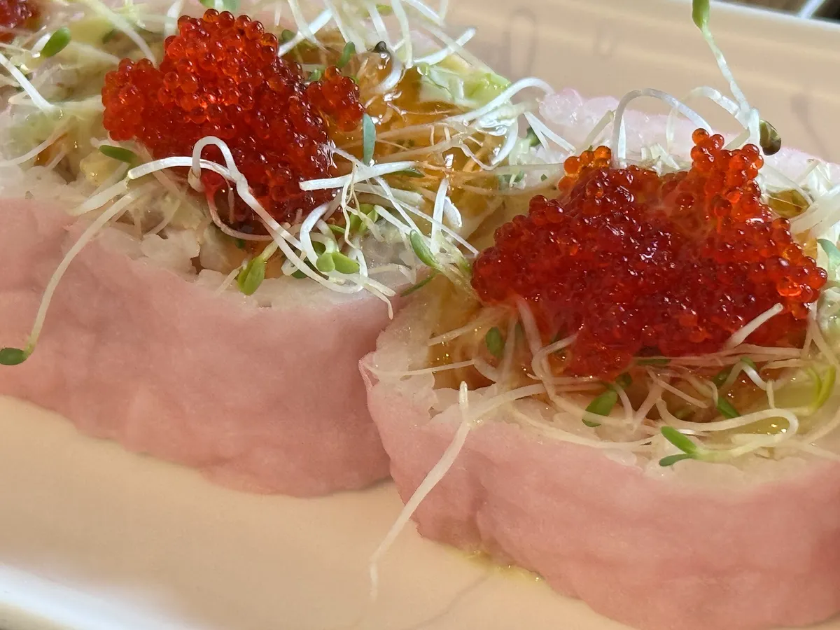 Pink sushi rolls topped with red caviar and sprouts
